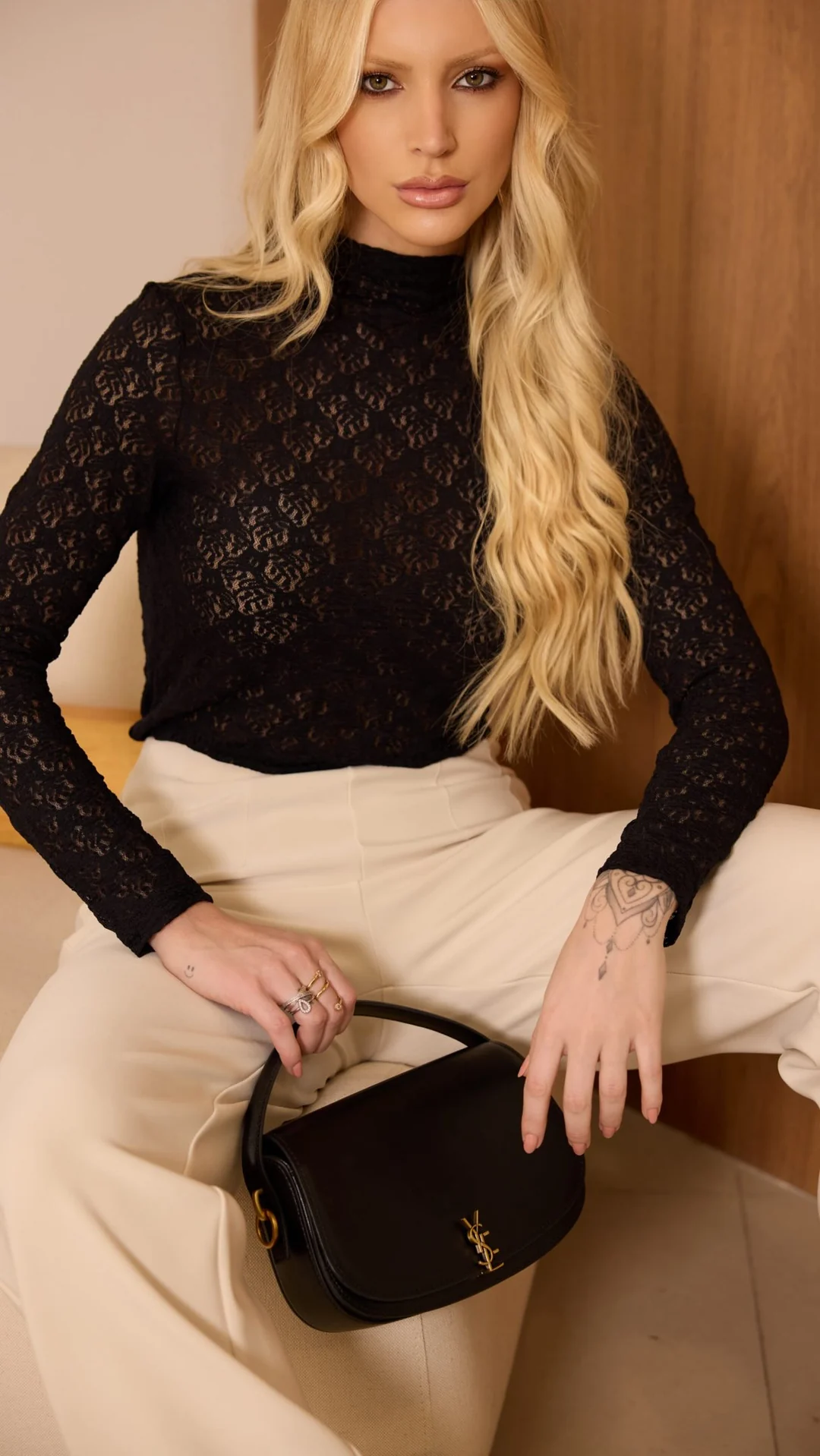 Duda Veiga sentada, com blusa preta de renda e calça bege